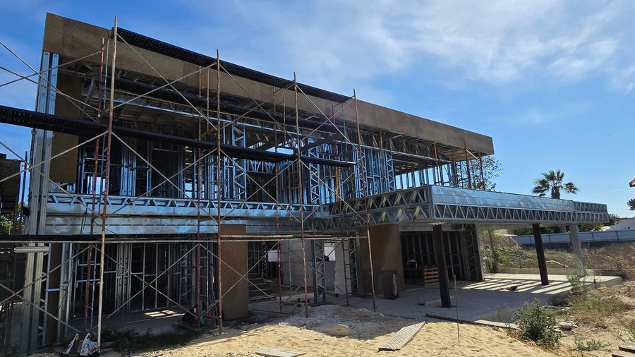 Moradia Oliveira em construção: estrutura em perfis de aço galvanizado montada
                  sobre a laje, com andaimes e paredes já revestidas a OSB.